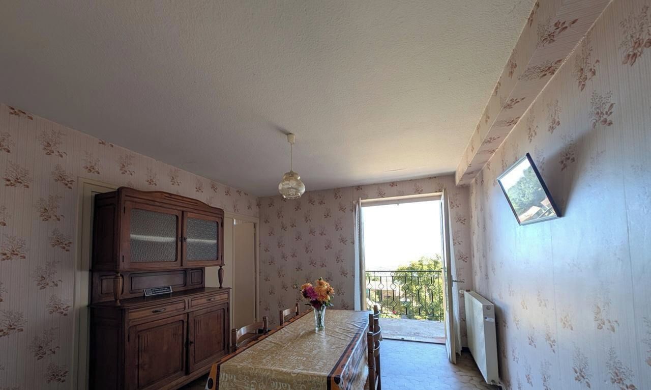 A dining area with a wooden cabinet, a table with a vase of flowers, and a view through a door to an outdoor balcony.