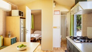 A compact kitchen with a stove, refrigerator, and a small dining area with a table and a bowl of apples. - Nice (sta)caravan in Pula with house sea view (Pula)