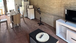 En rustik inredning med synliga träbjälkar, en tegelvägg, en matplats med ett dukat bord, en svart pall med en fjärrkontroll och ett vitt skåp med en tv.