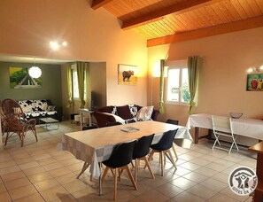 A dining area with a large table, chairs, and a sofa. There is a painting on the wall and a window with curtains. - Le Sabot - LES HAIES (LES HAIES)