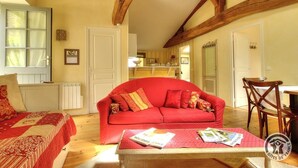 Uma sala de estar aconchegante com um sofá vermelho, uma mesa de centro de madeira com revistas, e vista para a cozinha.