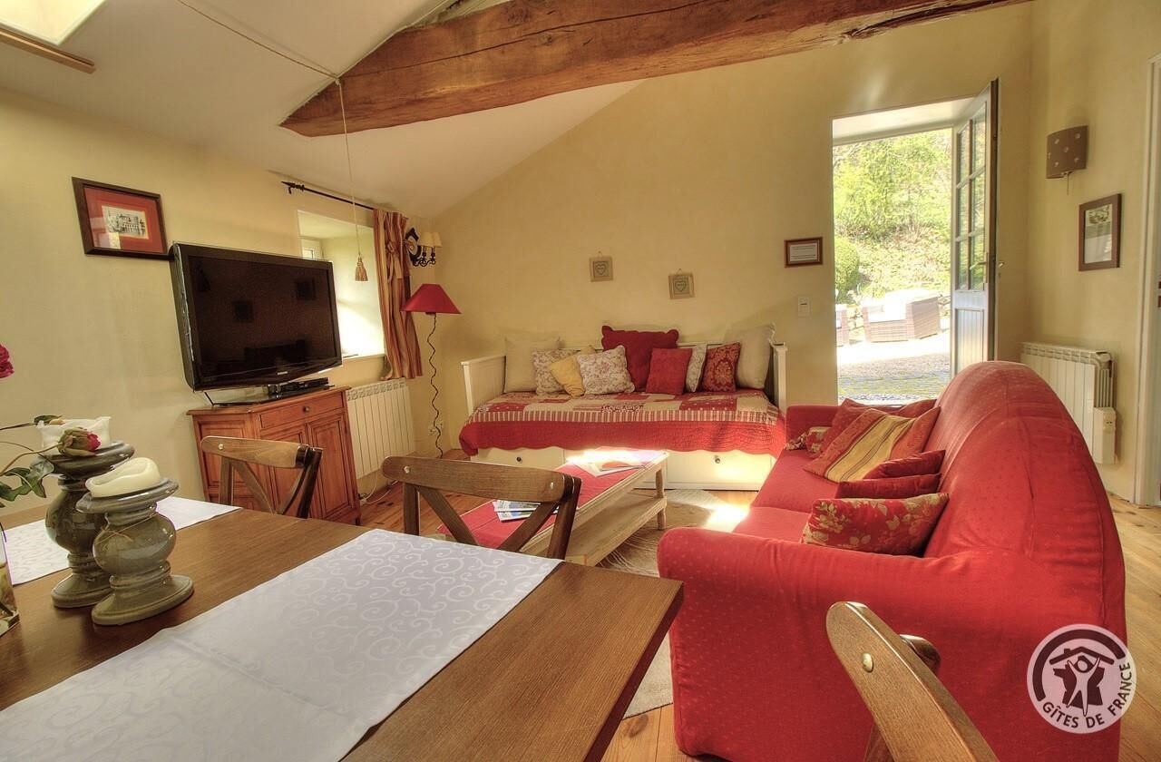 A cozy living room with a red sofa, a wooden dining table, and a television.