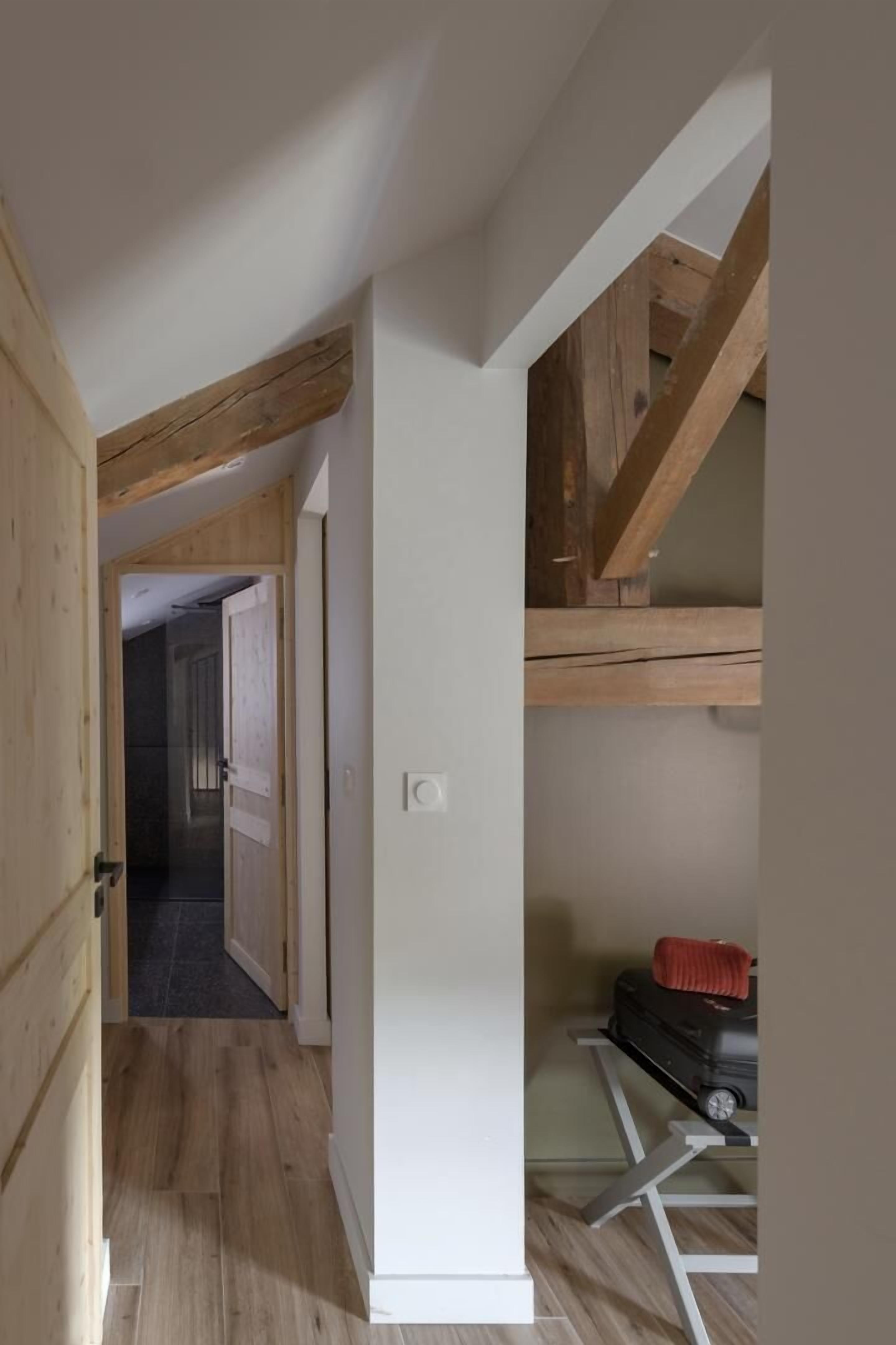 Un estrecho pasillo con vigas de madera, una pared blanca y una puerta que da a otra habitación.