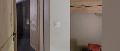 Un estrecho pasillo con vigas de madera, una pared blanca y una puerta que da a otra habitación.