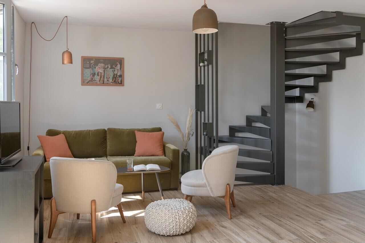 A modern living room with a sofa, two armchairs, a coffee table, and a staircase.
