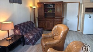 Ein Wohnzimmer mit einer Couch, zwei Ledersesseln, einem Holzschrank, einer Lampe und einem Kühlschrank.