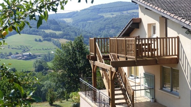 Ein zweistöckiges Haus mit einer Holzterrasse und einer Treppe, die zu einem Balkon führt.