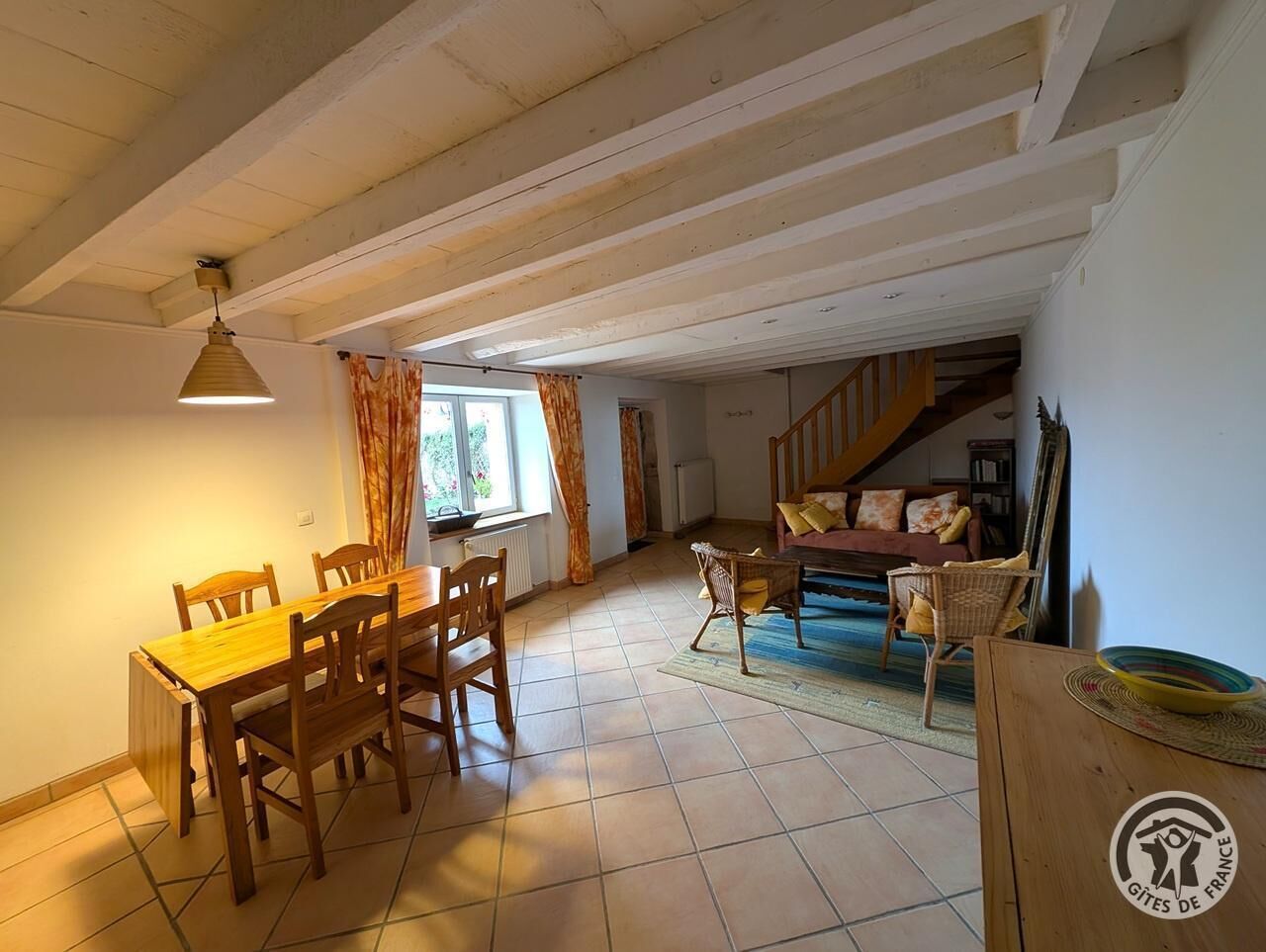 A spacious living area with a wooden dining table and chairs, a sofa, and a staircase leading to another level.
