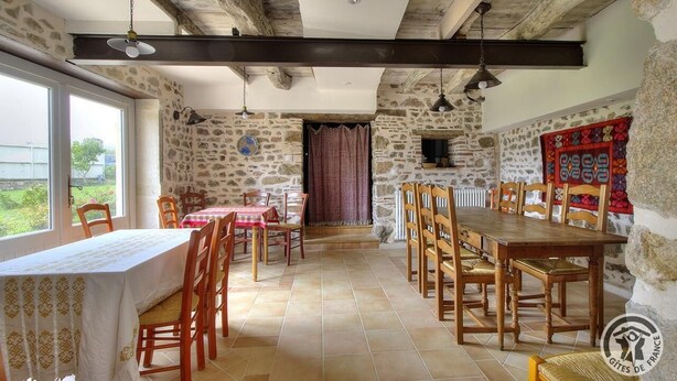 Un comedor con paredes de piedra, mesas y sillas de madera, y vistas a través de una ventana.