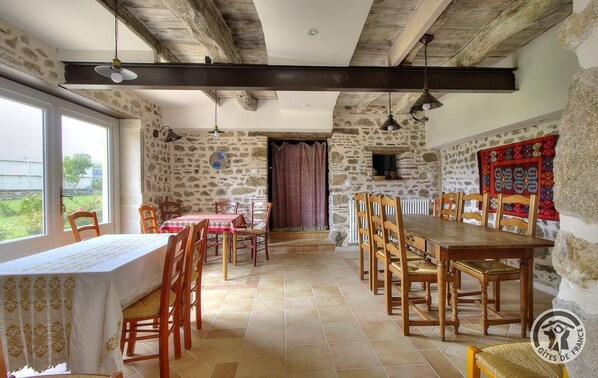 A dining area with stone walls, wooden tables and chairs, and a view through a window.