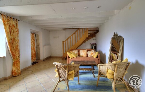 A spacious living room with a wooden staircase, a sofa with cushions, wicker chairs, and a large mirror.