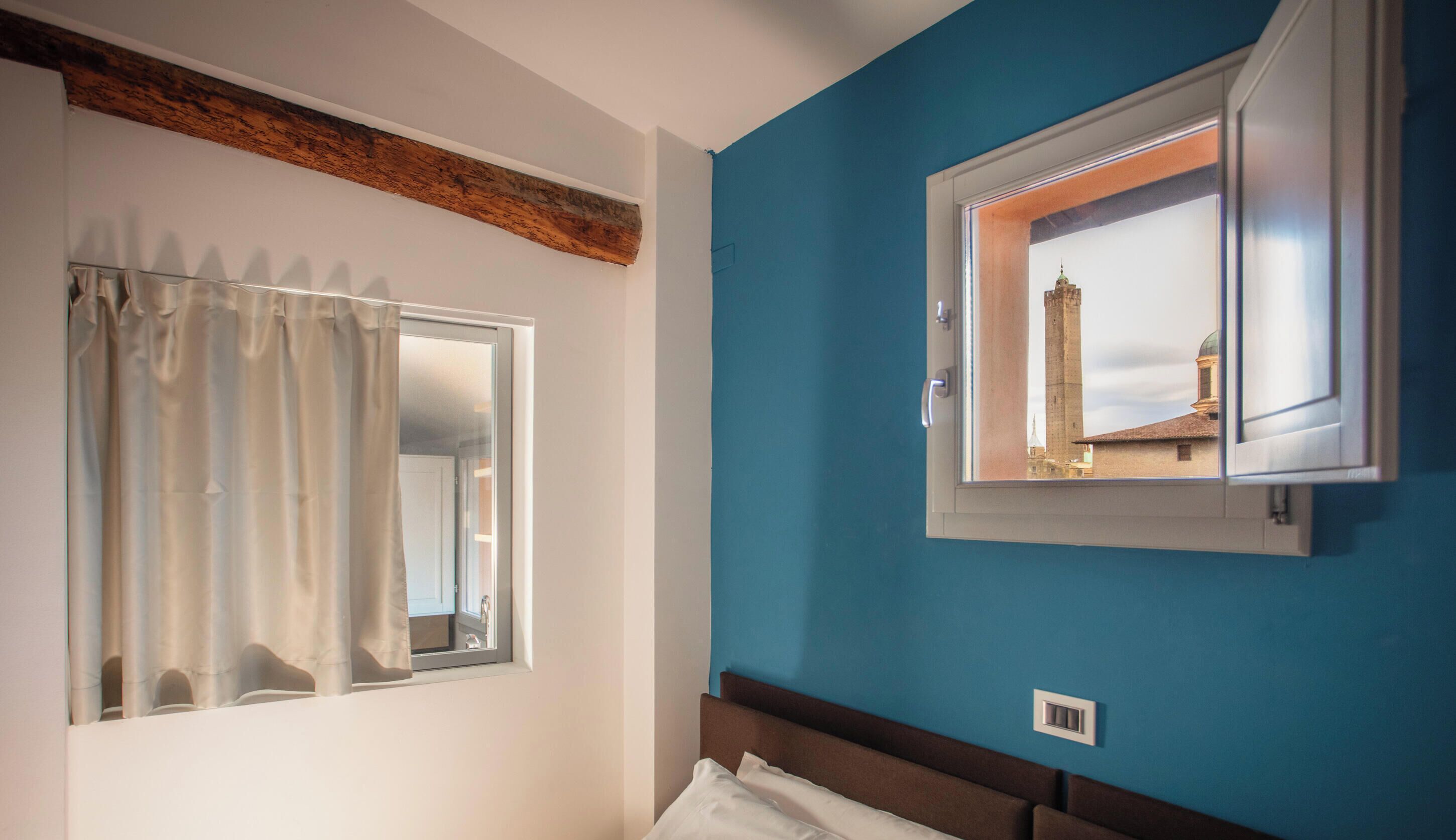 Une pièce avec une fenêtre, un miroir, un lit et une vue sur un immeuble par la fenêtre.