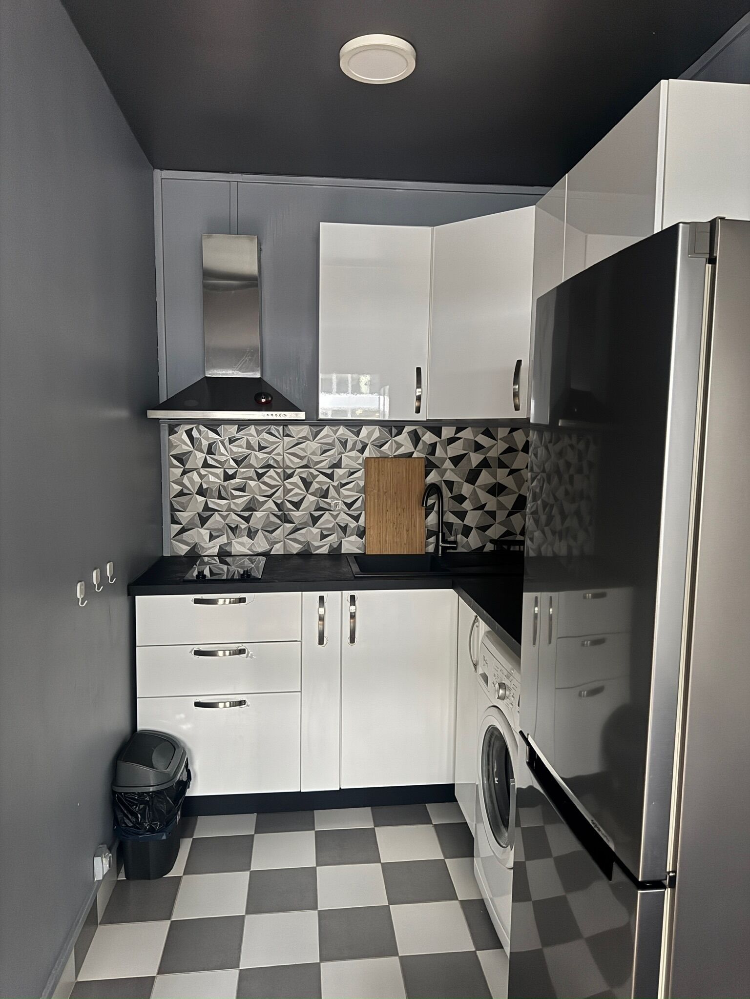 A compact kitchen with white cabinets, a black countertop, a built-in washing machine, and a checkered floor.
