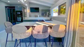 A modern kitchen with a central island, bar stools, and a large window with curtains.