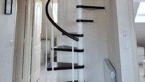 Una escalera de caracol con barandillas blancas y peldaños oscuros, que sube a un piso superior.