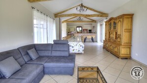 Ein geräumiges Wohnzimmer mit einem grauen Ecksofa, einer Holzkommode und einem Essbereich mit Tisch und Stühlen.