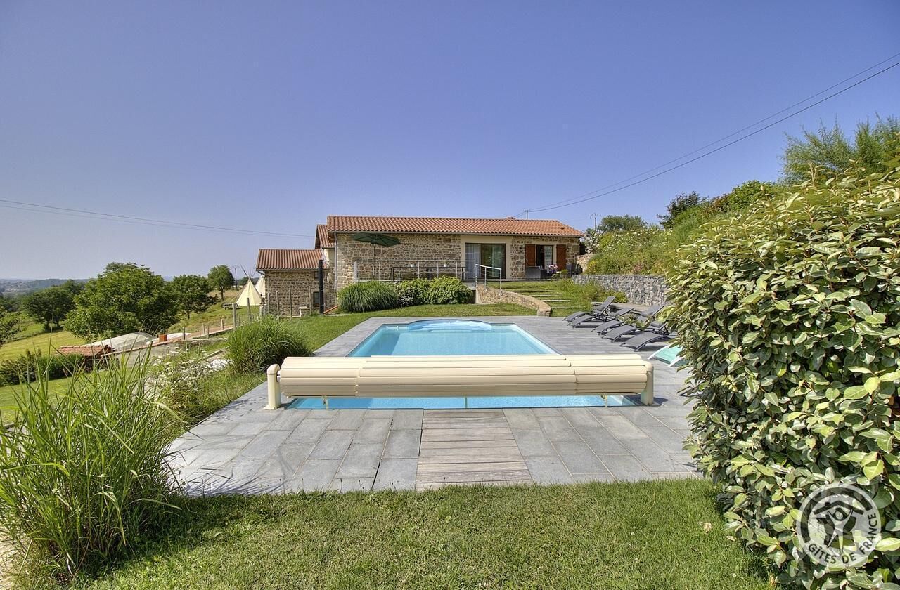 Une maison avec une piscine, une façade en pierre et un jardin bien entretenu.
