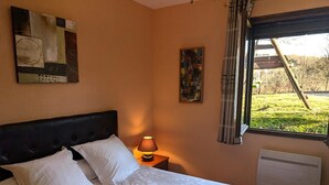 A bedroom with a bed, a nightstand with a lamp, a window with a view of the outdoors, and a radiator. - Les Griottes - SAIN-BEL (SAIN-BEL)