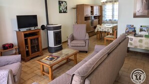 A cozy living room with a sofa, a television, a fireplace, and a dining area with a table and chairs. - Les Griottes - SAIN-BEL (SAIN-BEL)