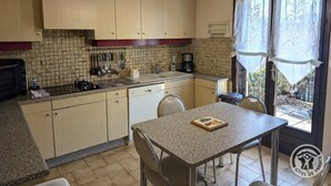 A compact kitchen with wooden cabinets, a granite countertop, a dining table, and a window with curtains. - Les Griottes - SAIN-BEL (SAIN-BEL)