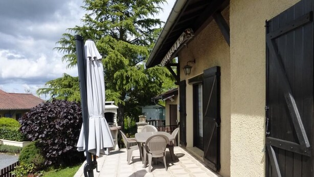 An outdoor patio with a table and chairs, a covered umbrella, and a garden area with plants and a fence. - Les Griottes - SAIN-BEL (SAIN-BEL)