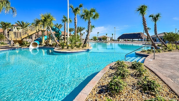 En swimmingpool med vandrutsjebaner, palmer og en bygning med stråtækt tag.