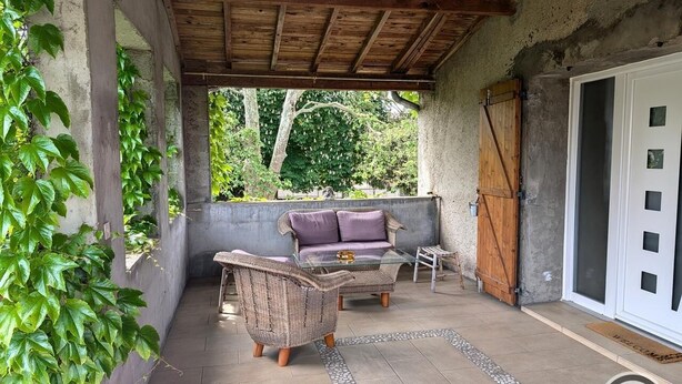 A covered patio area with wicker furniture, a glass table, and a door with a metal handle. - Citybreak Le Planier (SAINT PRIEST)