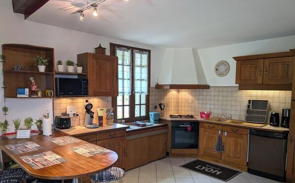A kitchen with wooden cabinets, a microwave, a stove, a sink, and a dining area with a table and chairs. - Citybreak Le Planier (SAINT PRIEST)