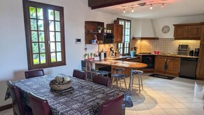 A kitchen with wooden cabinets, a dining table with chairs, a built-in stove, and a window with a view of greenery. - Citybreak Le Planier (SAINT PRIEST)