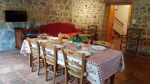 Zona pranzo con parete in pietra, divano rosso, sedie di legno, tavolo con tovaglia a quadri e televisione a parete.