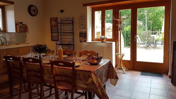 Zona pranzo con tavolo apparecchiato per quattro, sedie di legno, una finestra vista su vegetazione e una porta che dà sull'esterno.