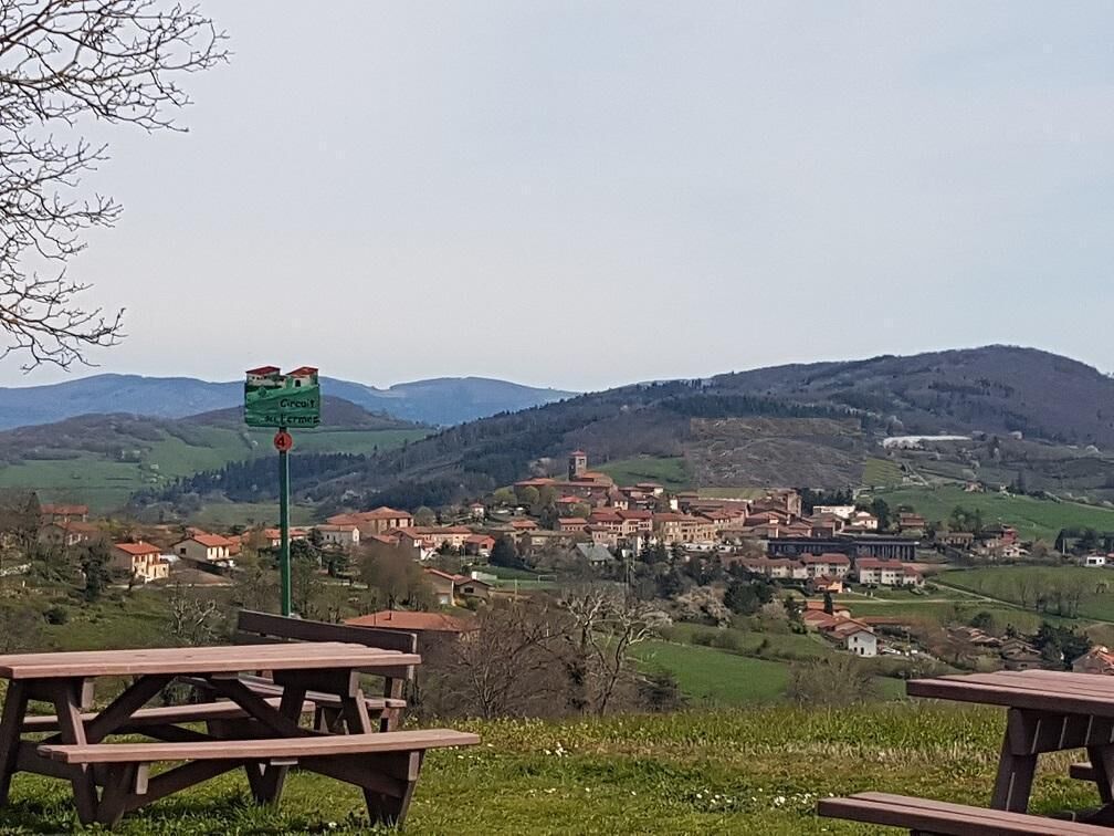 Ein ländliches Dorf mit einem Wegweiser, Picknicktischen und Blick auf die umliegenden Hügel.
