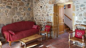 Una stanza con pareti in pietra, soffitto in legno, un divano rosso, un tavolo e una sedia di legno.