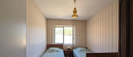 A room with two beds, a window, and a hanging light fixture.