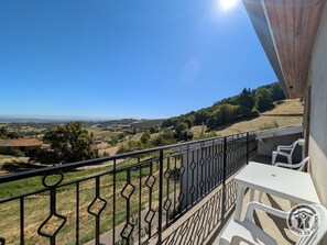 A balcony with a view of a rural landscape, a table with chairs, and a railing. - Gîte de la Panoncelière 2 (RONTALON)