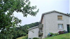 Un bâtiment à deux étages doté d’un balcon, entouré de verdure et situé au pied d’une colline.