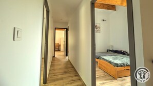 Un pasillo estrecho con suelo de madera que conduce a un dormitorio con cama y mesita de noche.