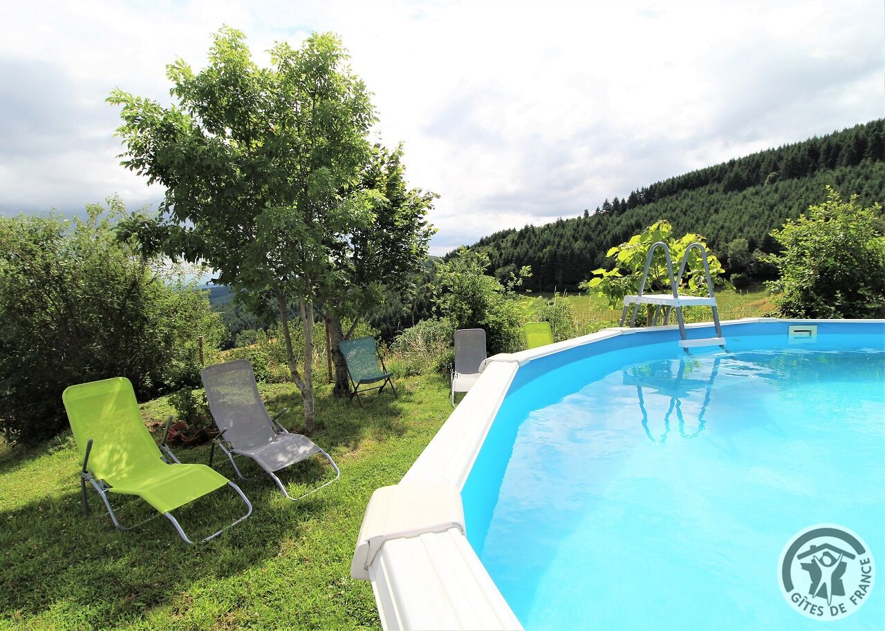 A swimming pool with a white deck, surrounded by green chairs and a tree.