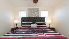 A bedroom with a tufted headboard, a striped bedspread, two bedside lamps, and a wall-mounted painting. - Rooftop Pool & Iconic Views | Chic Hollywood Apt (Los Angeles)