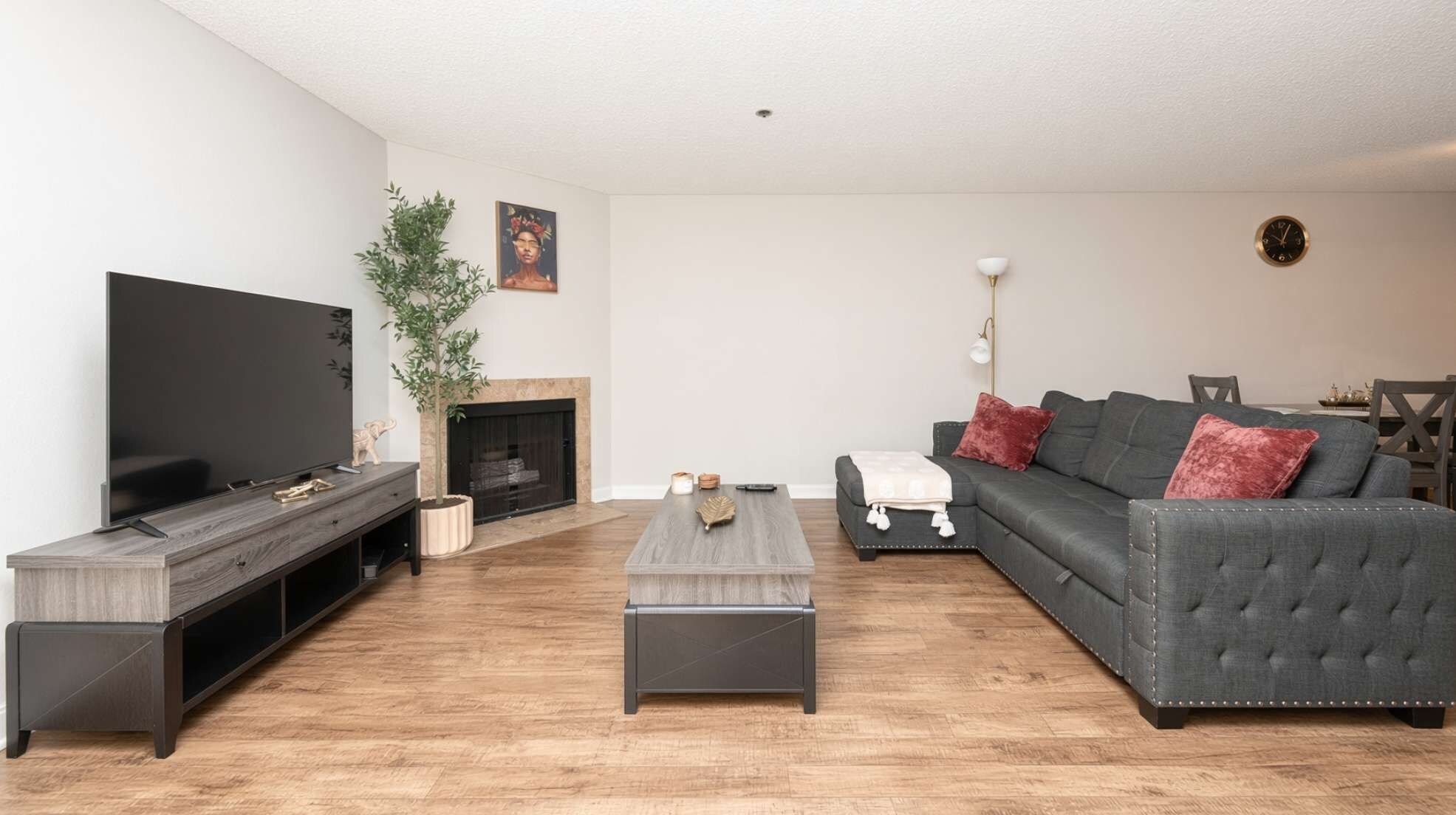 A modern living room with a flat-screen TV, dark wood flooring, a grey sofa with red cushions, a coffee table, and a fireplace.