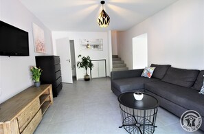 A modern living room with a grey sofa, a wooden bench, a round black coffee table, and a ceiling light fixture. - Les Romatières - CHAPONNAY (CHAPONNAY)