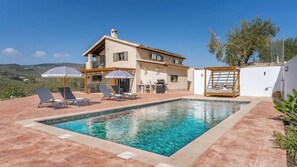Une maison à deux étages avec une piscine, un espace salon extérieur et une vue sur la campagne.