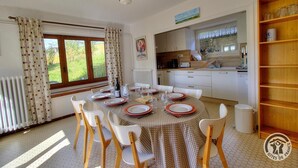 A dining area with a round table set for four, white chairs, a ceiling fan, and a view of the garden through large windows. - Gîte de Haute Combe - JULIENAS (JULIENAS)