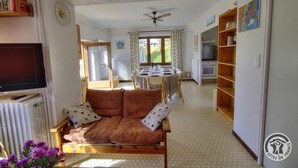 A living room with a sofa, a television, a dining area with a table and chairs, and a kitchen area with a stove. - Gîte de Haute Combe - JULIENAS (JULIENAS)