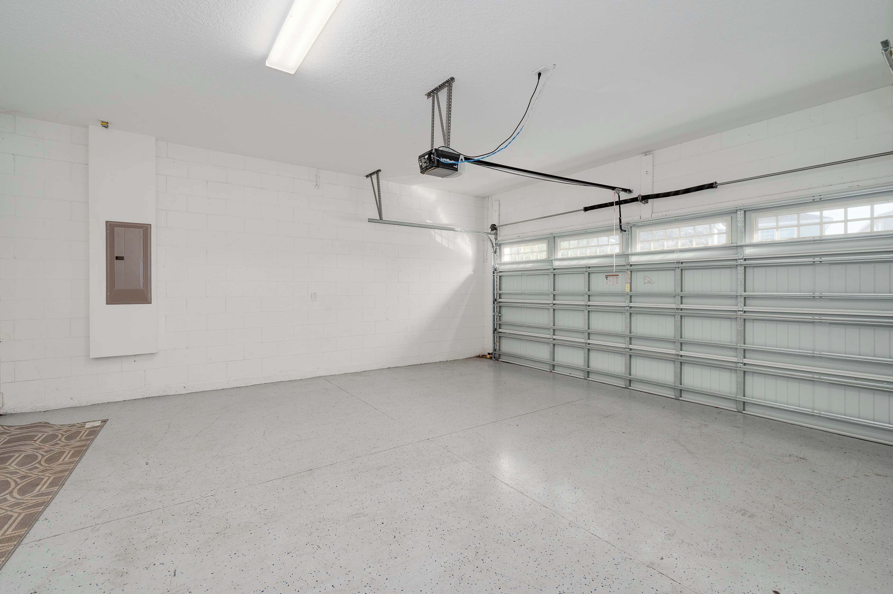 A clean, empty garage with a white floor, a metal garage door, and a ceiling-mounted projector.
