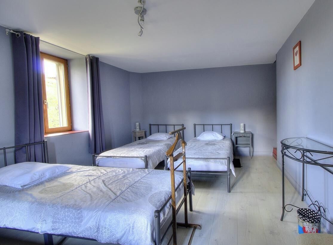 Un dormitori amb tres llits, una taula de metall i una finestra amb cortines.
