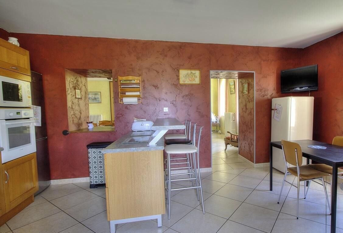 A kitchen with a central island, bar stools, a dining table, and a TV mounted on the wall.