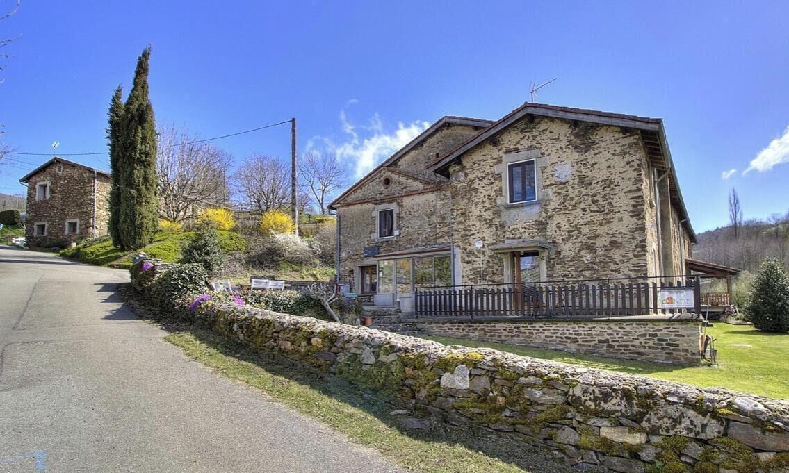 A stone building with a porch, a stone wall, and a clear sky.