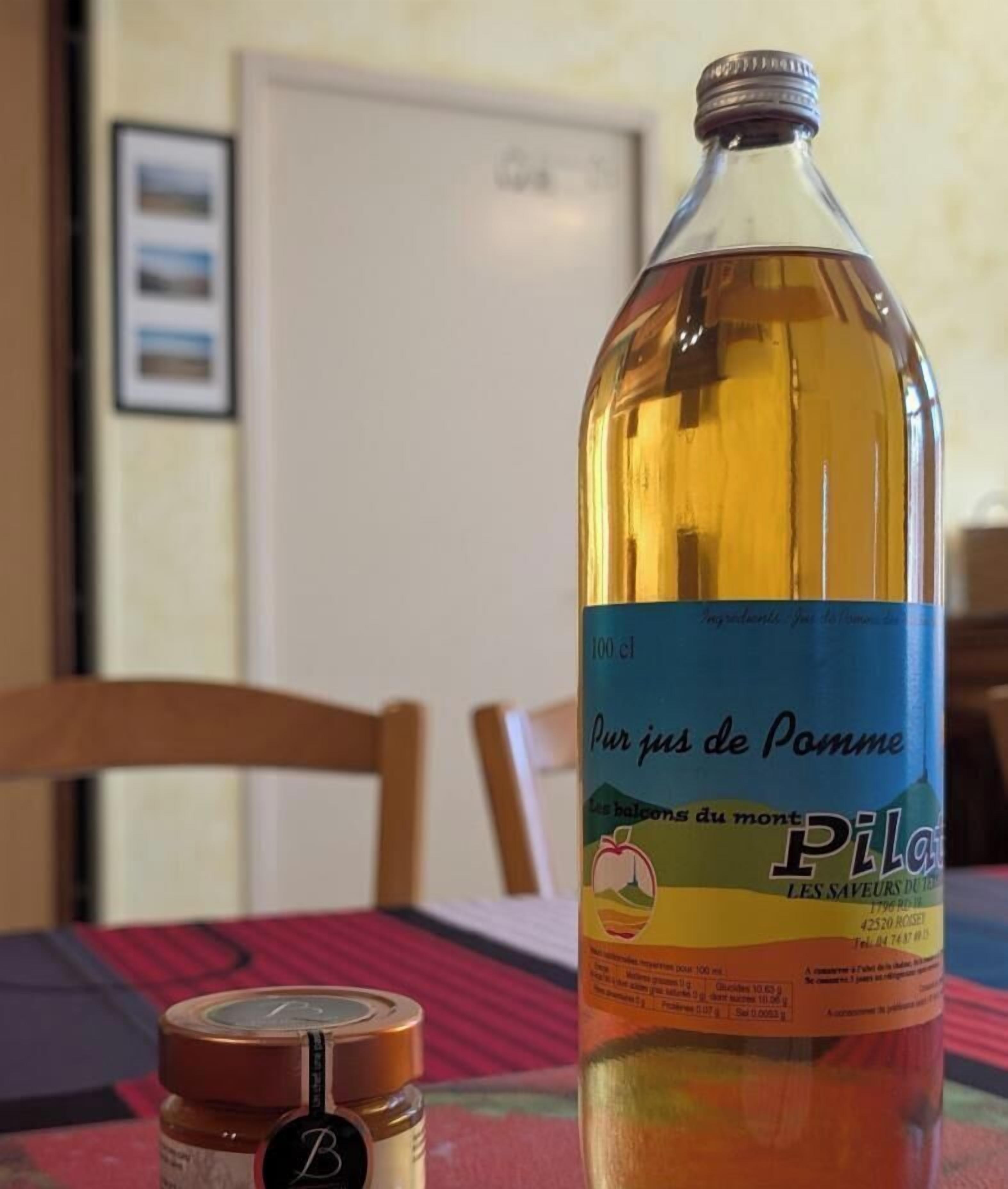 Une bouteille de cidre de pomme est posée sur une table, à côté d’une chaise en bois et d’un tableau encadré accroché au mur.