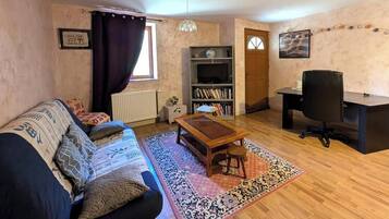 Una sala de estar con un sofá, una mesa de centro de madera, un mueble para la televisión y un escritorio con una silla.
